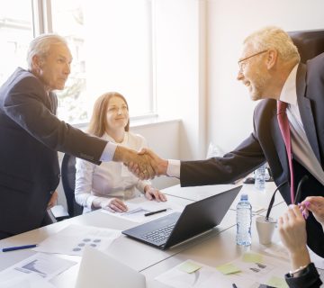 Smiling woman looking two senior businessman shaking hands 360x320
