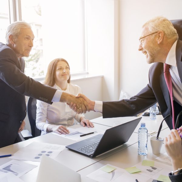 Smiling woman looking two senior businessman shaking hands 600x600